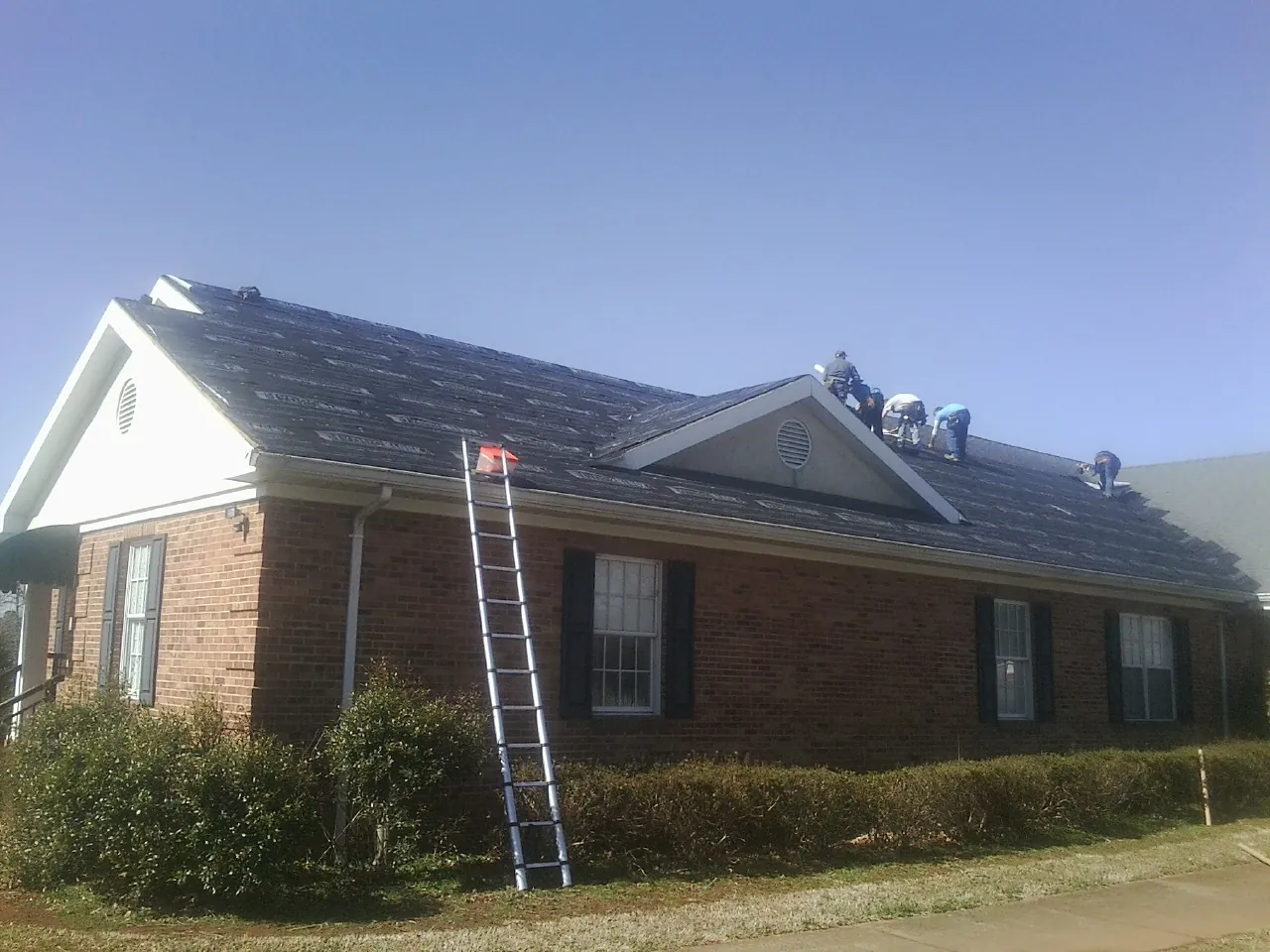 Crew tearing shingles off a brick ranch roof with a ladder set — Emergency Roof Repair work by our crew in Saint Joseph