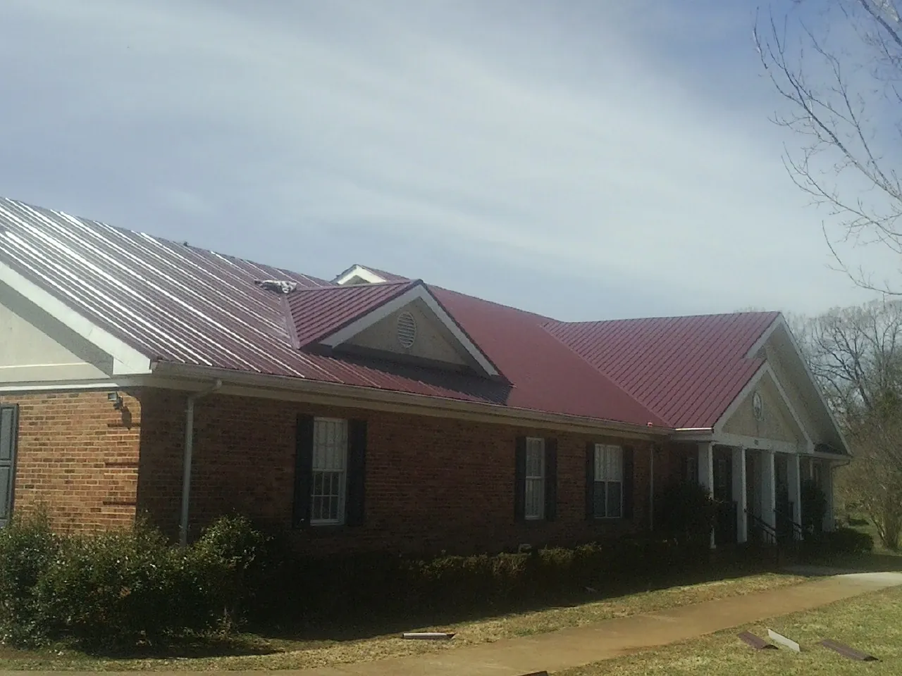 Red metal roof with gabled entries on a long brick building, from a Hail Damage Roof Repair job in Saint Joseph