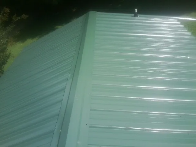 New green metal panels meeting at the ridge of a roof — Flat Roof Repair work by our crew in Saint Joseph
